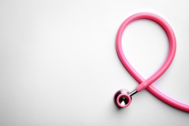 Photo of Pink stethoscope folded like awareness ribbon on white background, top view with space for text. Breast cancer concept