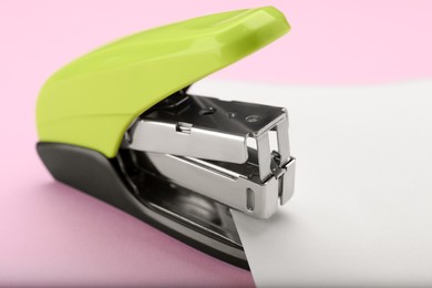 Photo of New bright stapler with paper sheet on pink background, closeup