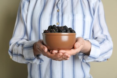 Woman holding bowl of fresh ripe black mulberries on light grey background, closeup