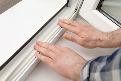 Photo of Worker putting rubber draught strip onto window indoors, closeup