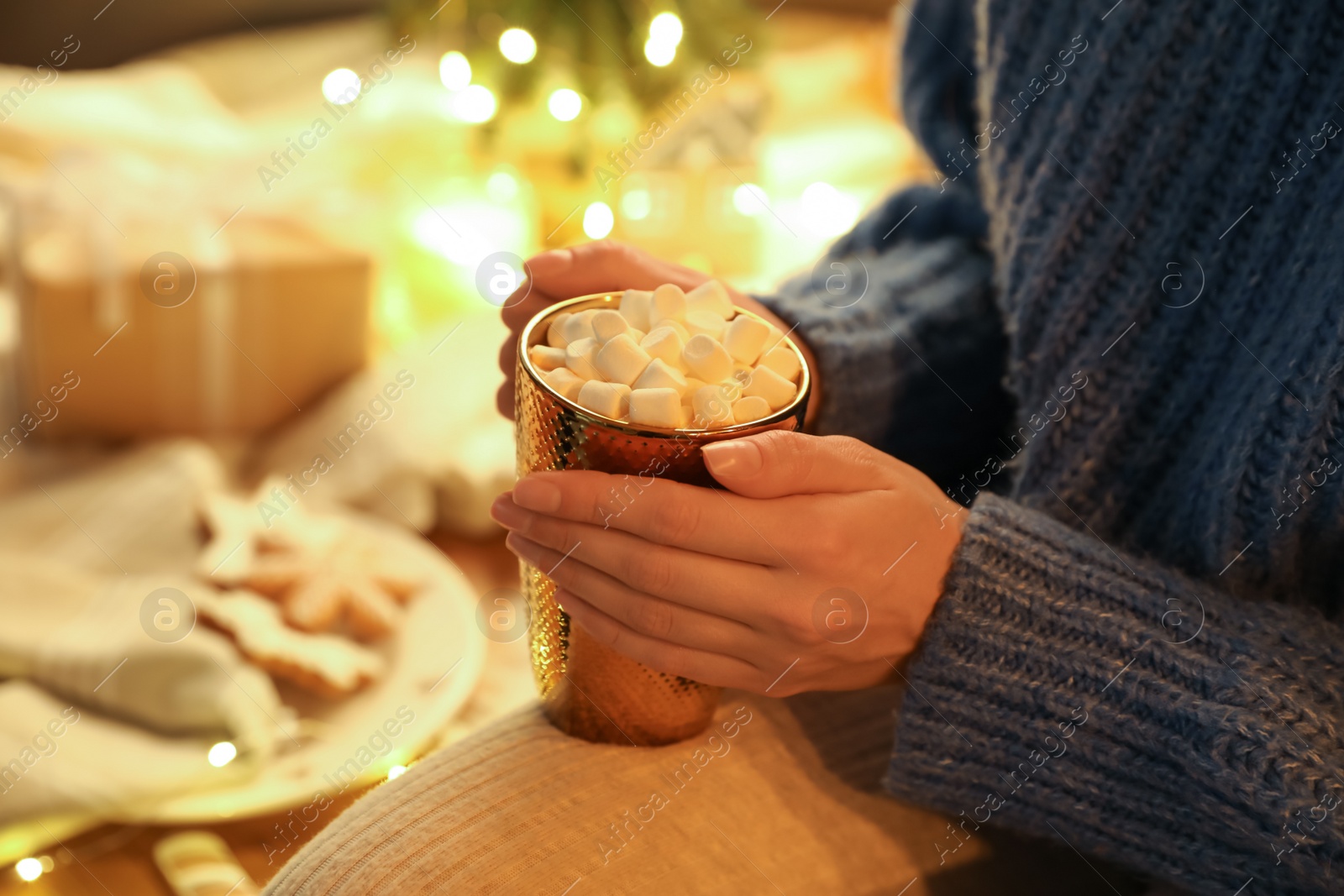 Photo of Woman holding cup of hot drink with marshmallows indoors, closeup. Magic Christmas atmosphere