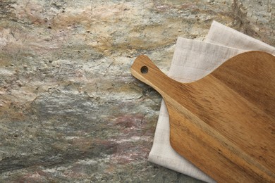 Photo of Wooden cutting board and napkin on textured table, top view. Space for text