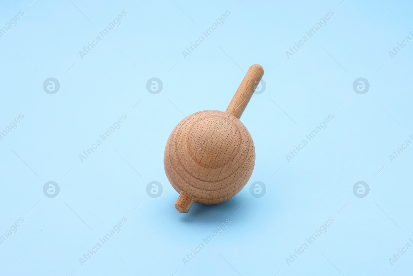 Photo of One wooden spinning top on light blue background. Toy whirligig