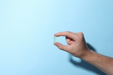 Photo of Man holding pill on light blue background, closeup. Space for text
