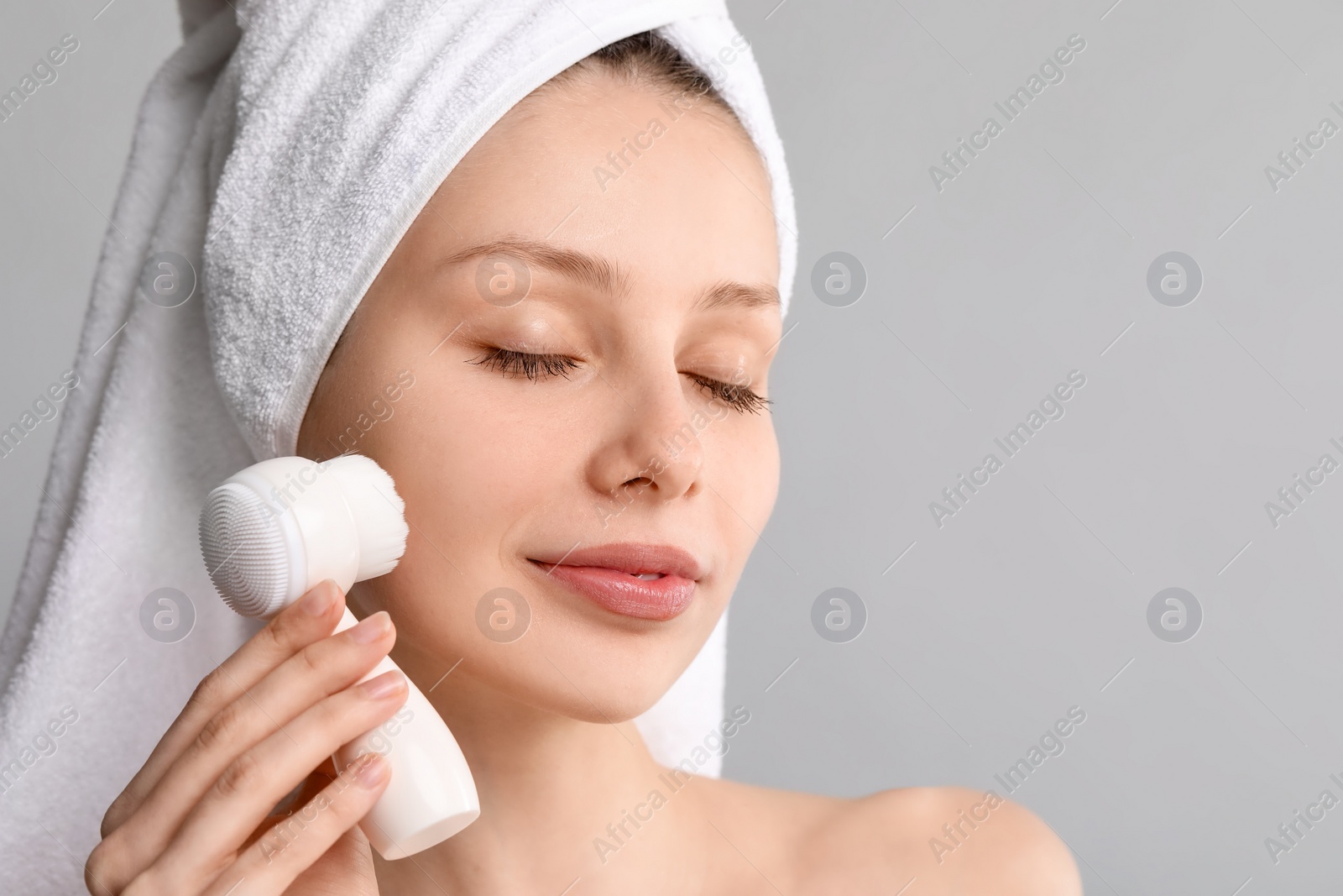 Photo of Washing face. Young woman with cleansing brush on grey background, closeup. Space for text