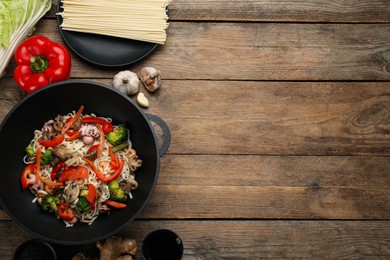 Stir fried noodles with mushrooms, seafood and vegetables in wok on wooden table, flat lay. Space for text