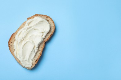 Photo of Slice of bread with tasty cream cheese on light blue background, top view. Space for text