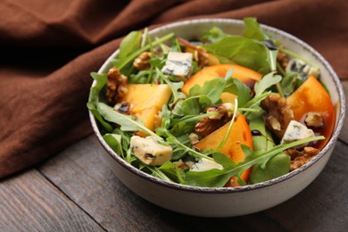Photo of Tasty salad with persimmon, blue cheese and walnuts served on wooden table, closeup. Space for text