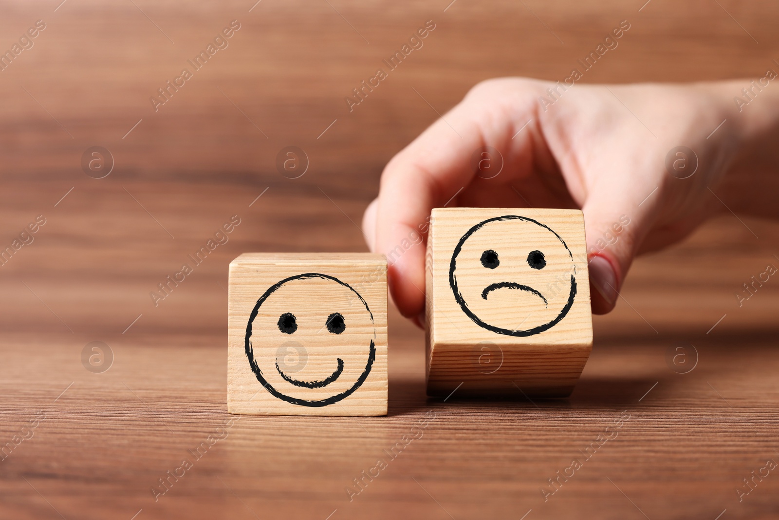Image of Complaint. Woman choosing cube with drawn sad face instead of another one with happy on wooden table, closeup