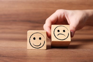 Complaint. Woman choosing cube with drawn sad face instead of another one with happy on wooden table, closeup