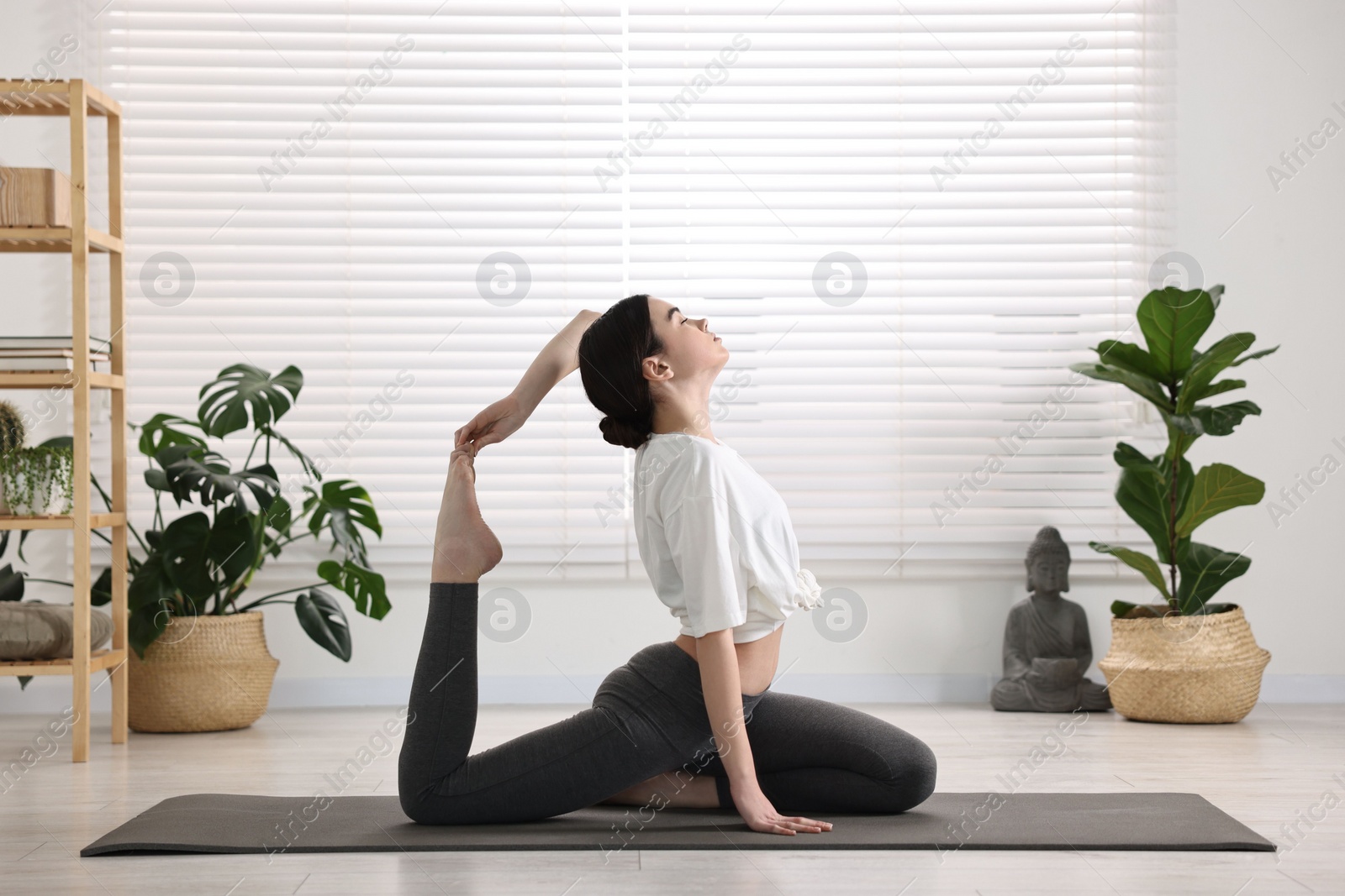 Photo of GIrl practicing one legged king pigeon asana on mat in yoga studio. Eka pada rajakapotasana pose