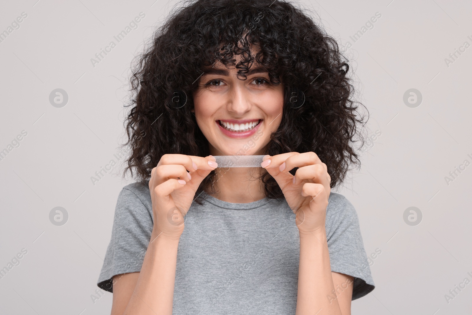 Photo of Young woman holding teeth whitening strip on light grey background