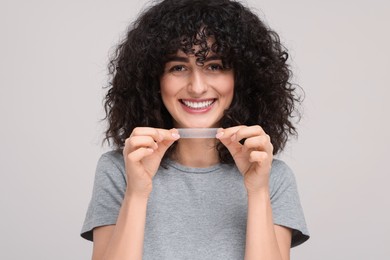 Photo of Young woman holding teeth whitening strip on light grey background