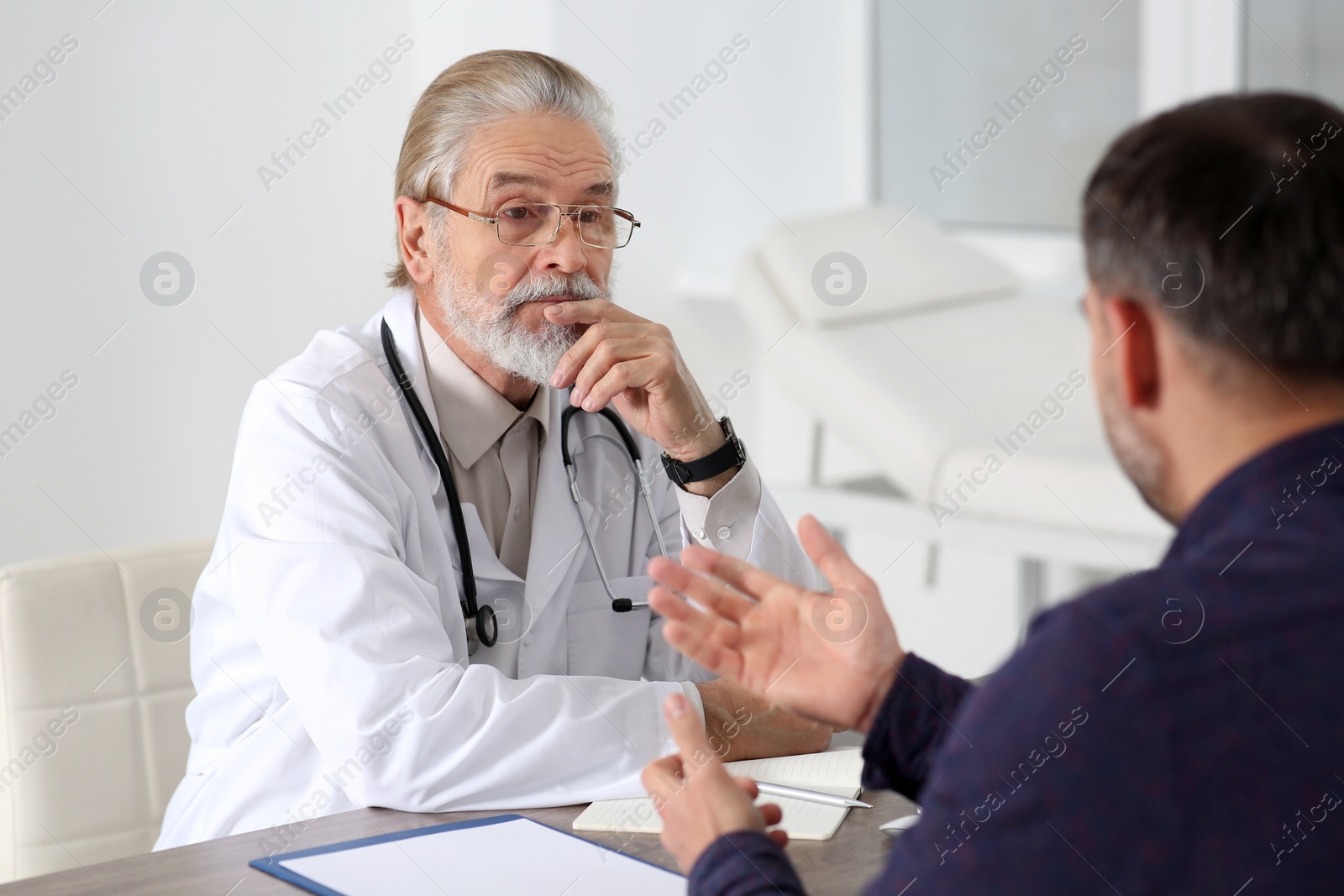 Photo of Senior doctor consulting patient at wooden table in clinic