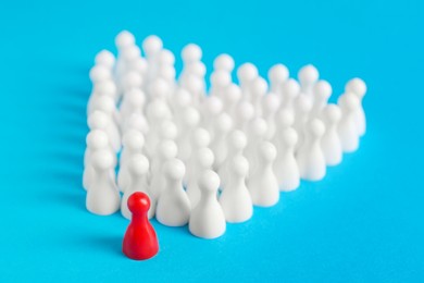 Photo of White pawns following red one on light blue background. Social inclusion concept