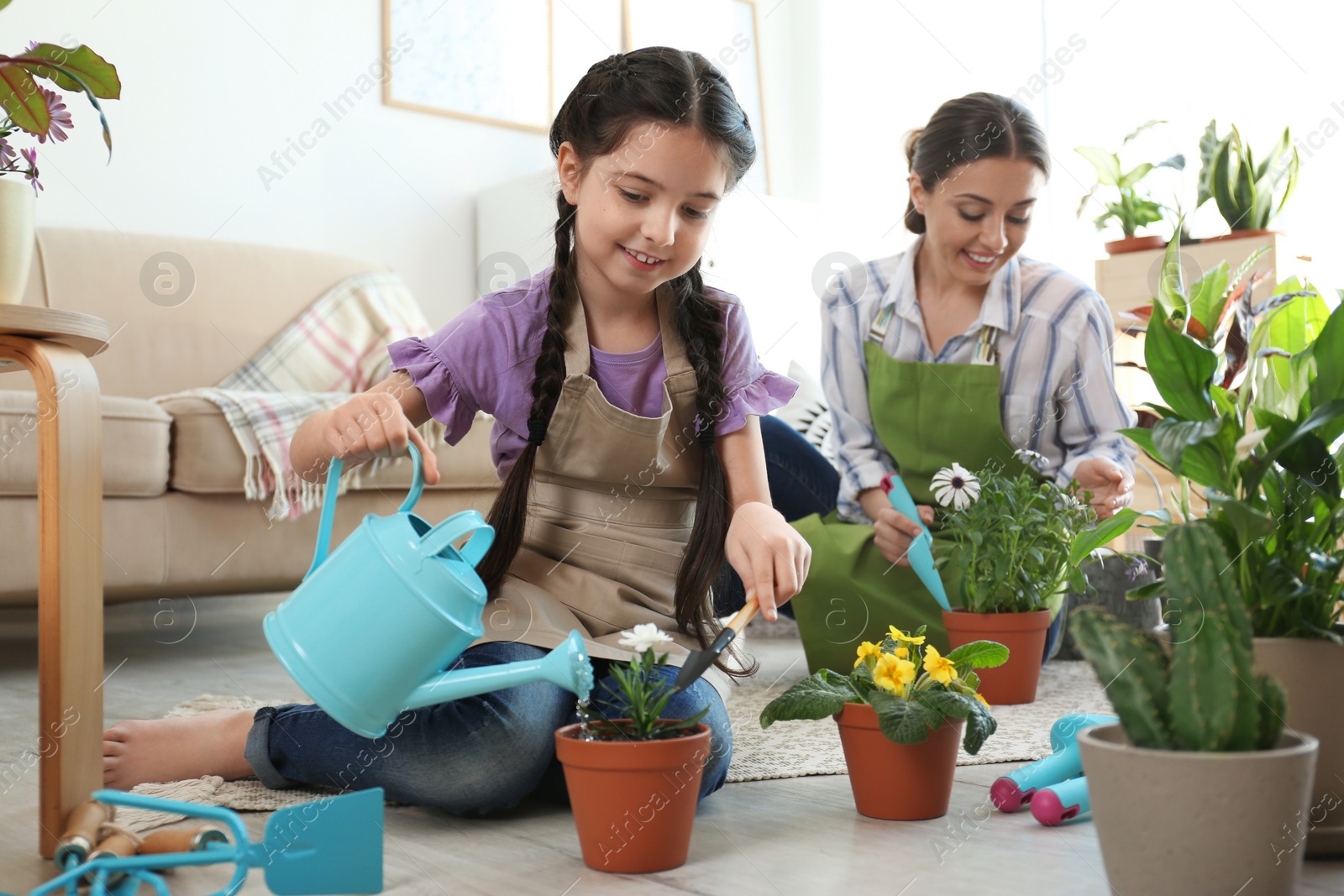 Photo of Mother and daughter taking care of potted plants on floor at home