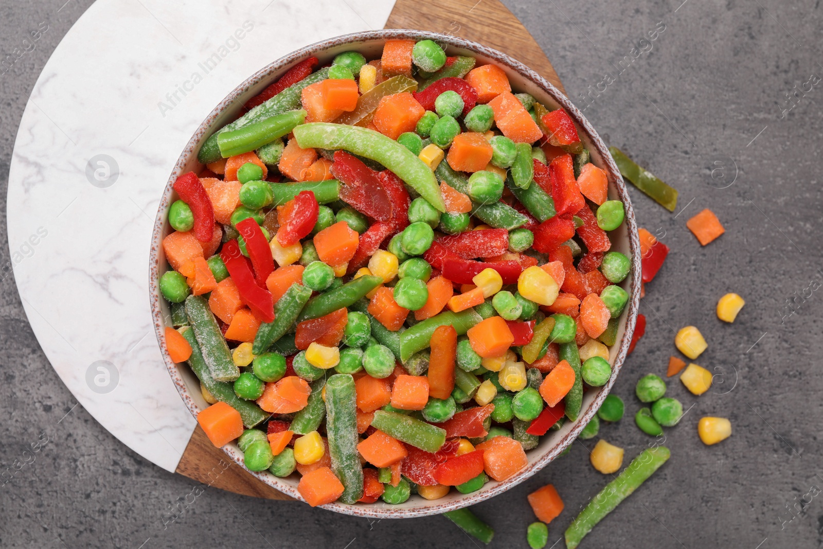 Photo of Mix of different frozen vegetables in bowl on grey table, top view