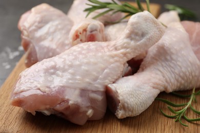 Raw chicken drumsticks with rosemary on wooden board, closeup