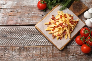 Photo of Delicious French fries with bacon, cheese sauce, tomatoes and herbs on wooden table, flat lay. Space for text