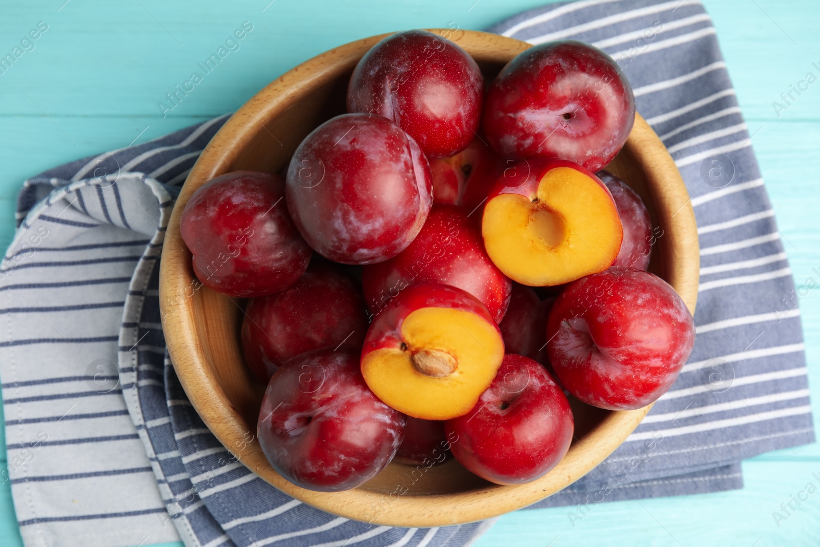 Photo of Delicious ripe plums in bowl on light blue wooden table, top view