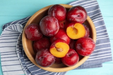 Delicious ripe plums in bowl on light blue wooden table, top view