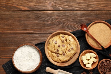 Photo of Fresh dough and different ingredients for cooking chocolate chip cookies on wooden table, flat lay. Space for text