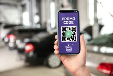 Image of Woman holding smartphone with activated promo code in car dealership, closeup