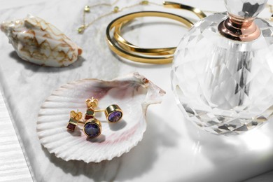 Photo of Different elegant bijouterie, shells and bottle of perfume on white table, closeup