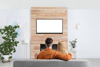 Photo of Couple watching TV on sofa in living room with decorative fireplace