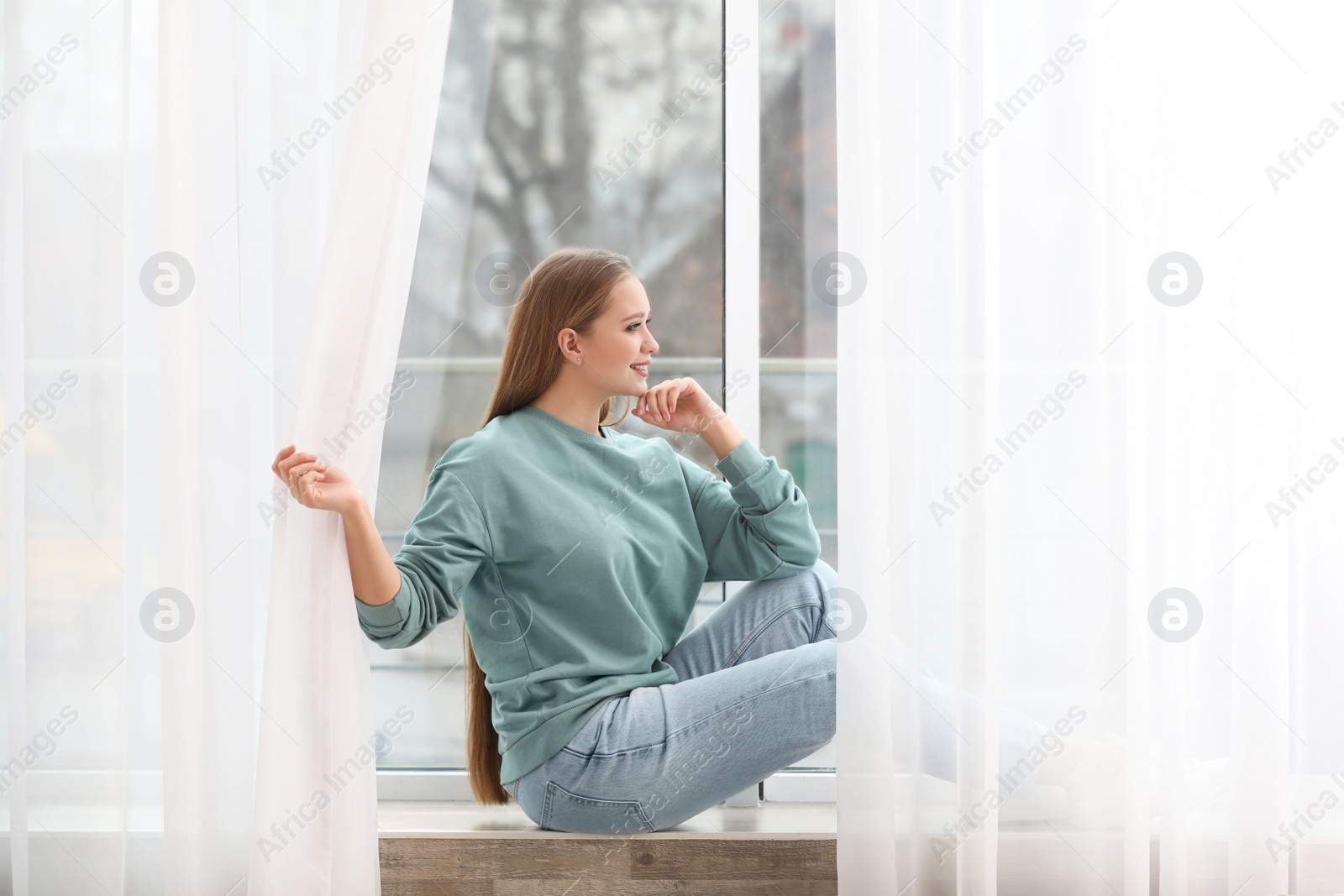 Photo of Beautiful young woman looking out of window at home