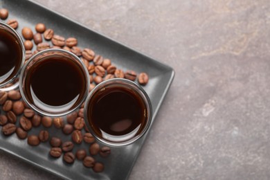 Shot glasses with coffee liqueur and beans on light grey table, top view. Space for text