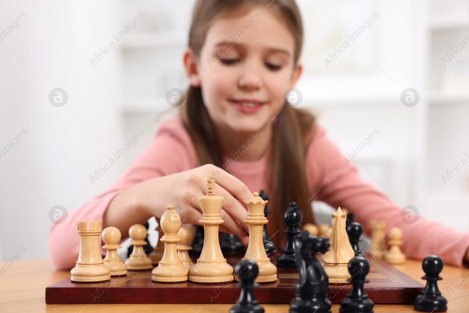 Photo of Cute girl playing chess at table indoors, selective focus