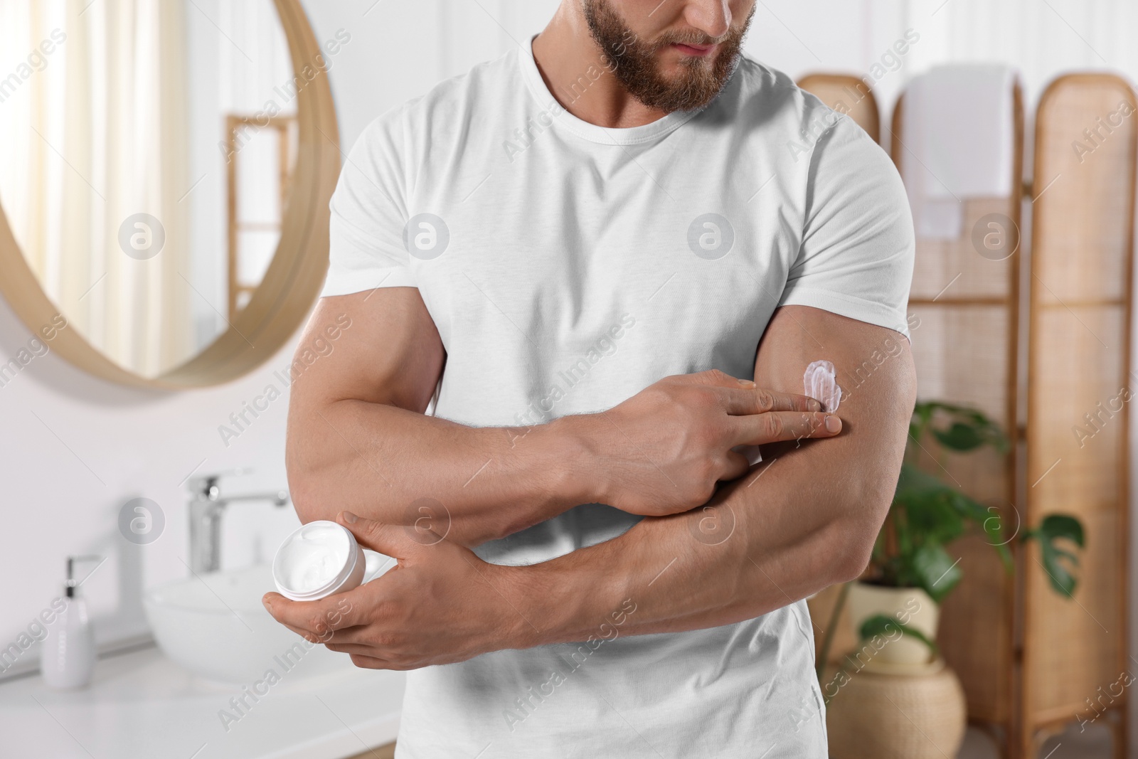 Photo of Man applying body cream onto his arm in bathroom, closeup