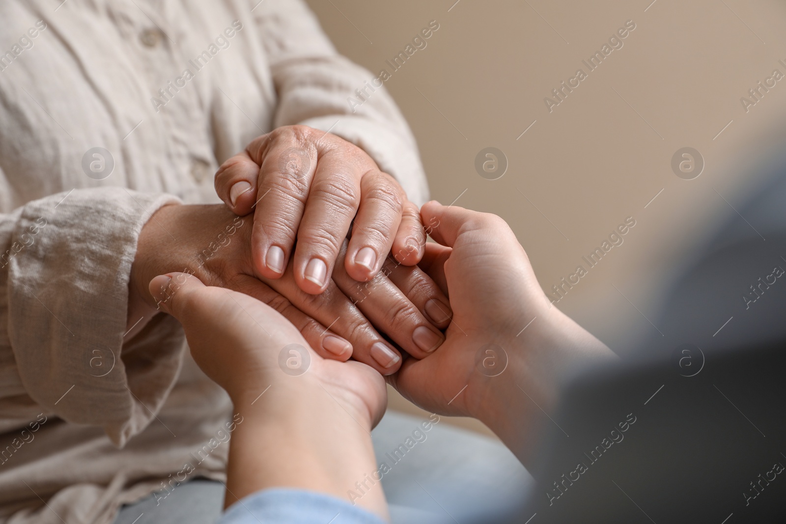 Photo of Woman holding hands with her mother on beige background, closeup