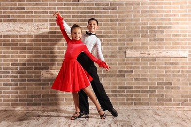 Photo of Beautifully dressed couple of kids dancing together near brick wall indoors