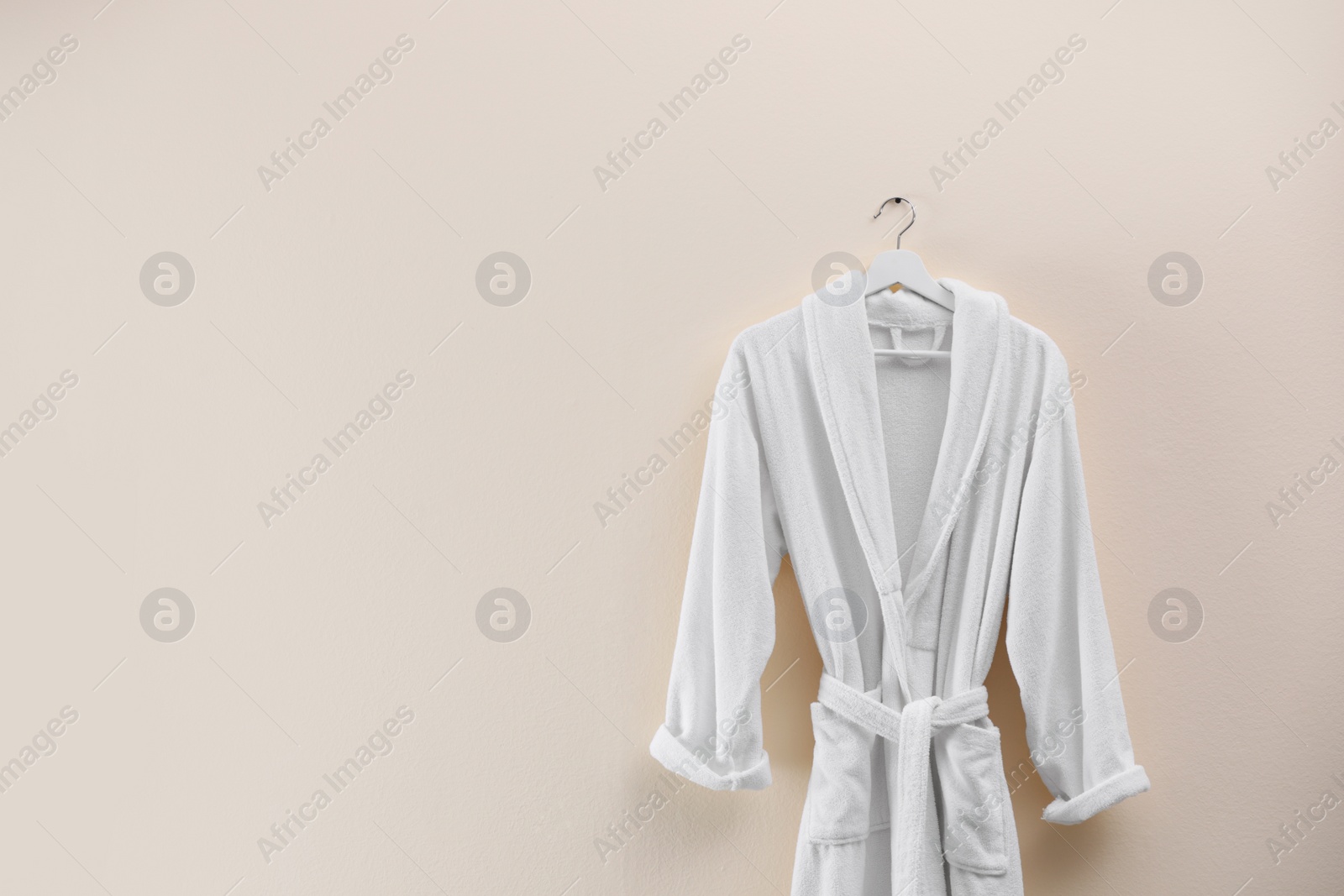 Photo of Soft comfortable bathrobe hanging on beige wall, space for text