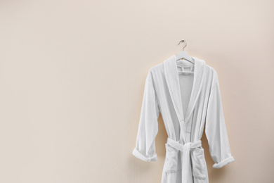 Soft comfortable bathrobe hanging on beige wall, space for text
