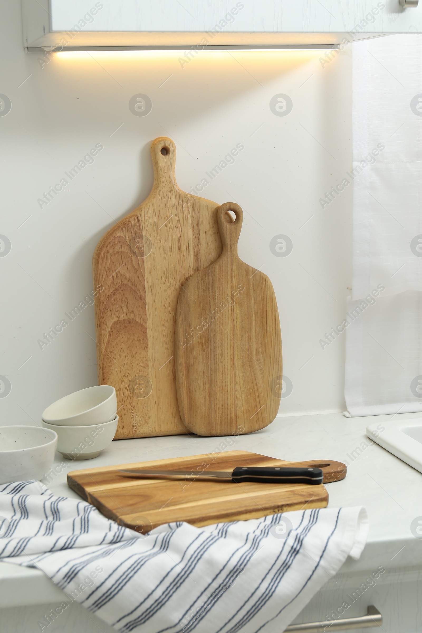 Photo of Wooden cutting boards, bowls, knife and towel on white countertop in kitchen