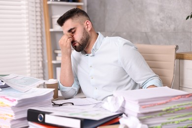 Photo of Overwhelmed man surrounded by documents at workplace in office