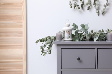 Photo of Stylish chest of drawers decorated with beautiful eucalyptus garland and candles indoors