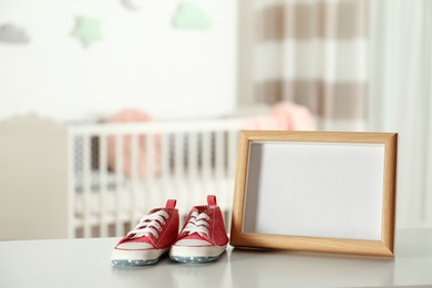 Photo frame and bootees on table in baby room interior. Space for text