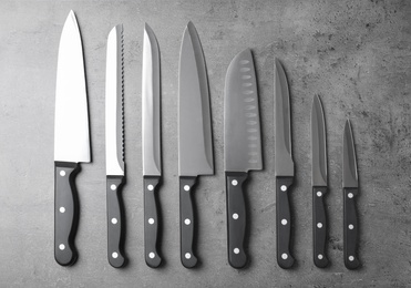 Photo of Set of sharp knives on grey background, flat lay