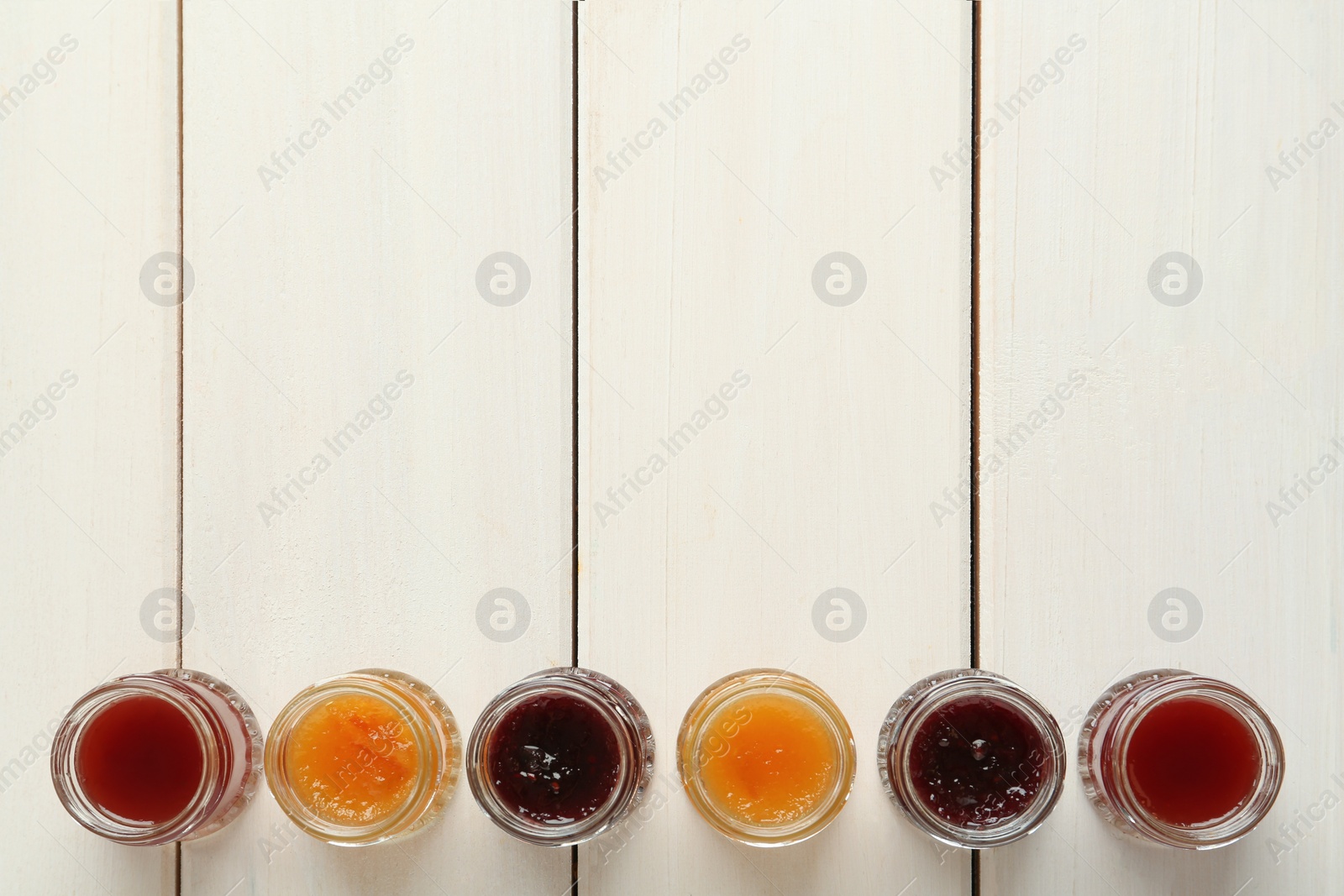 Photo of Jars of different jams on white wooden table, flat lay. Space for text