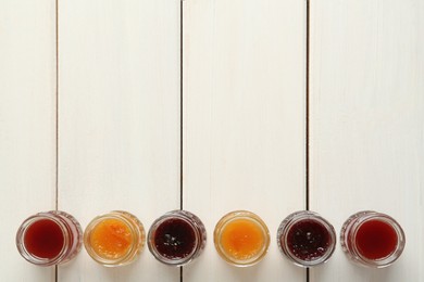 Jars of different jams on white wooden table, flat lay. Space for text