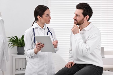 Photo of Doctor with tablet consulting patient during appointment in clinic