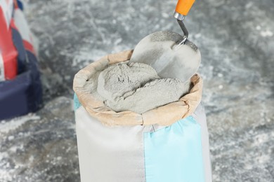 Photo of Cement powder and trowel put in bag on stone floor, closeup