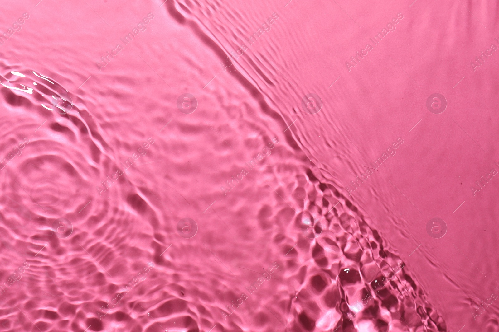 Photo of Rippled surface of clear water on bright pink background, top view