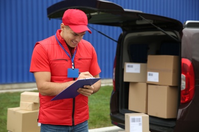 Courier with clipboard near car outdoors, space for text