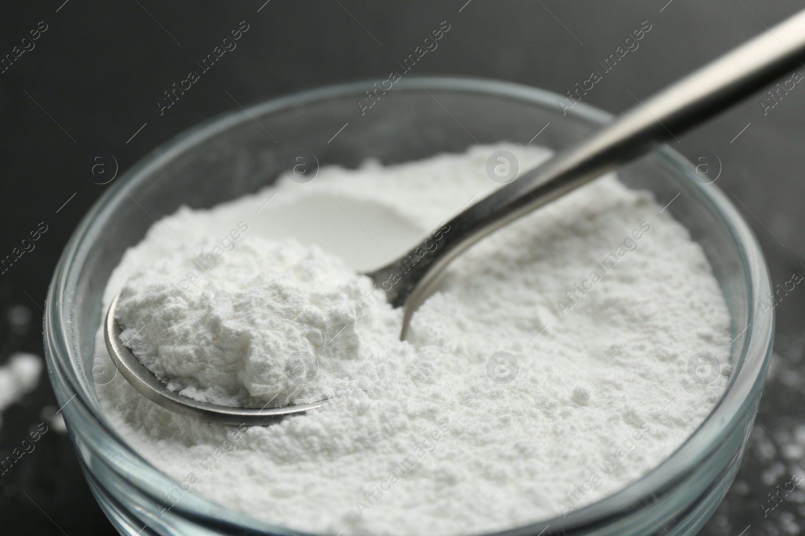 Photo of Baking powder in bowl and spoon on black table, closeup