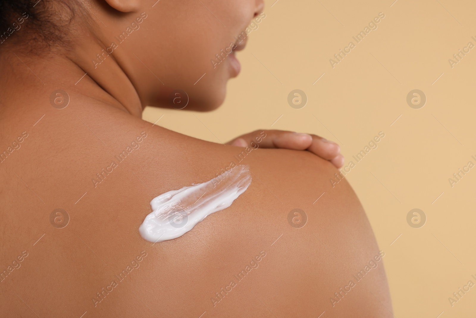 Photo of Young woman applying body cream onto back on beige background, closeup